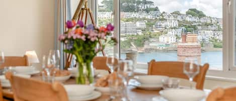 A dining table set for four with a view of a coastal town through large windows.