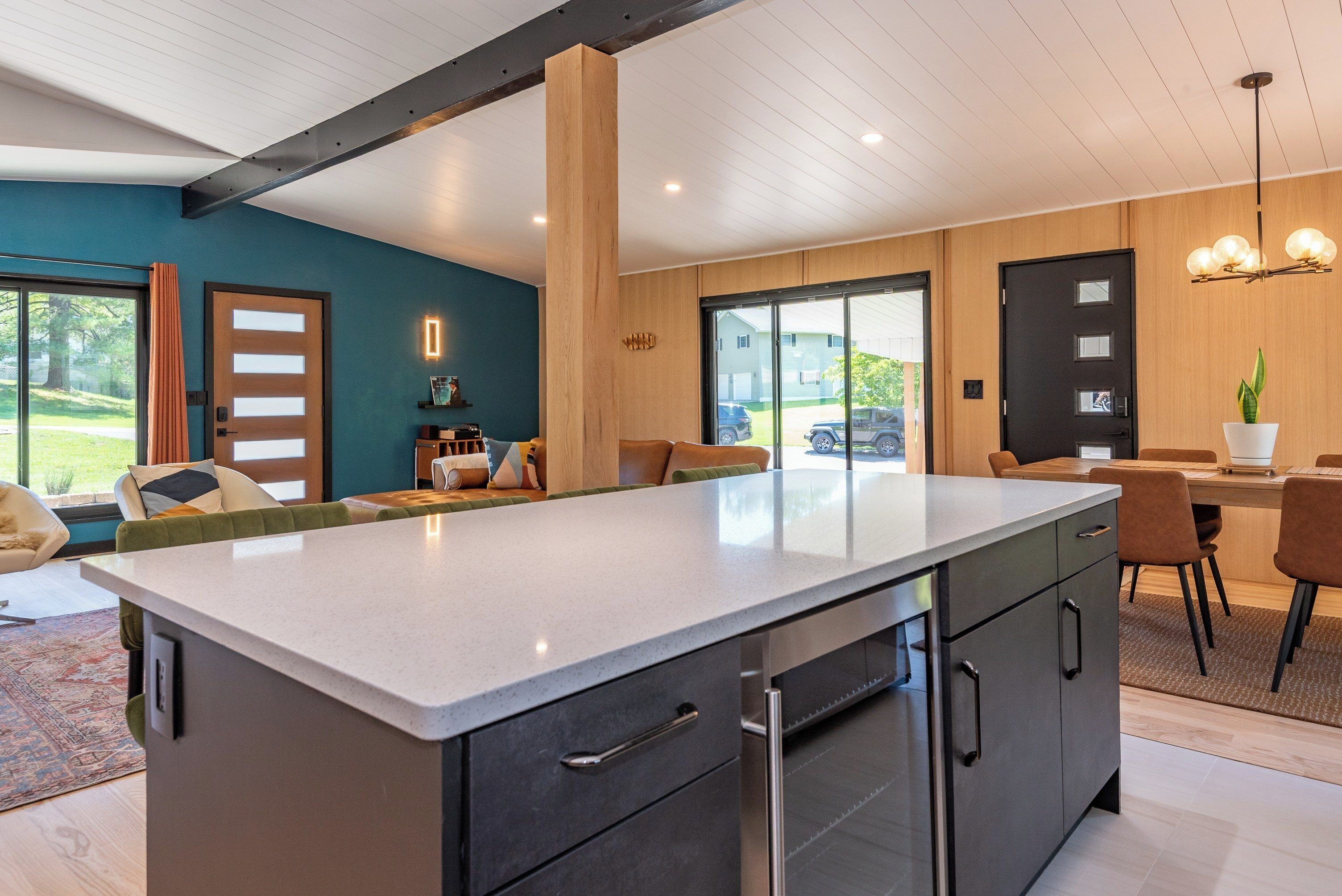 A modern kitchen with a large island, wooden cabinets, and a dining area with chairs and a table.