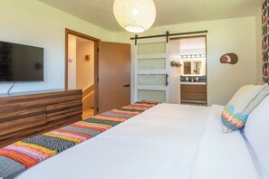 A bedroom with a bed, a TV, a wooden dresser, a colorful rug, and a sliding door leading to a bathroom.