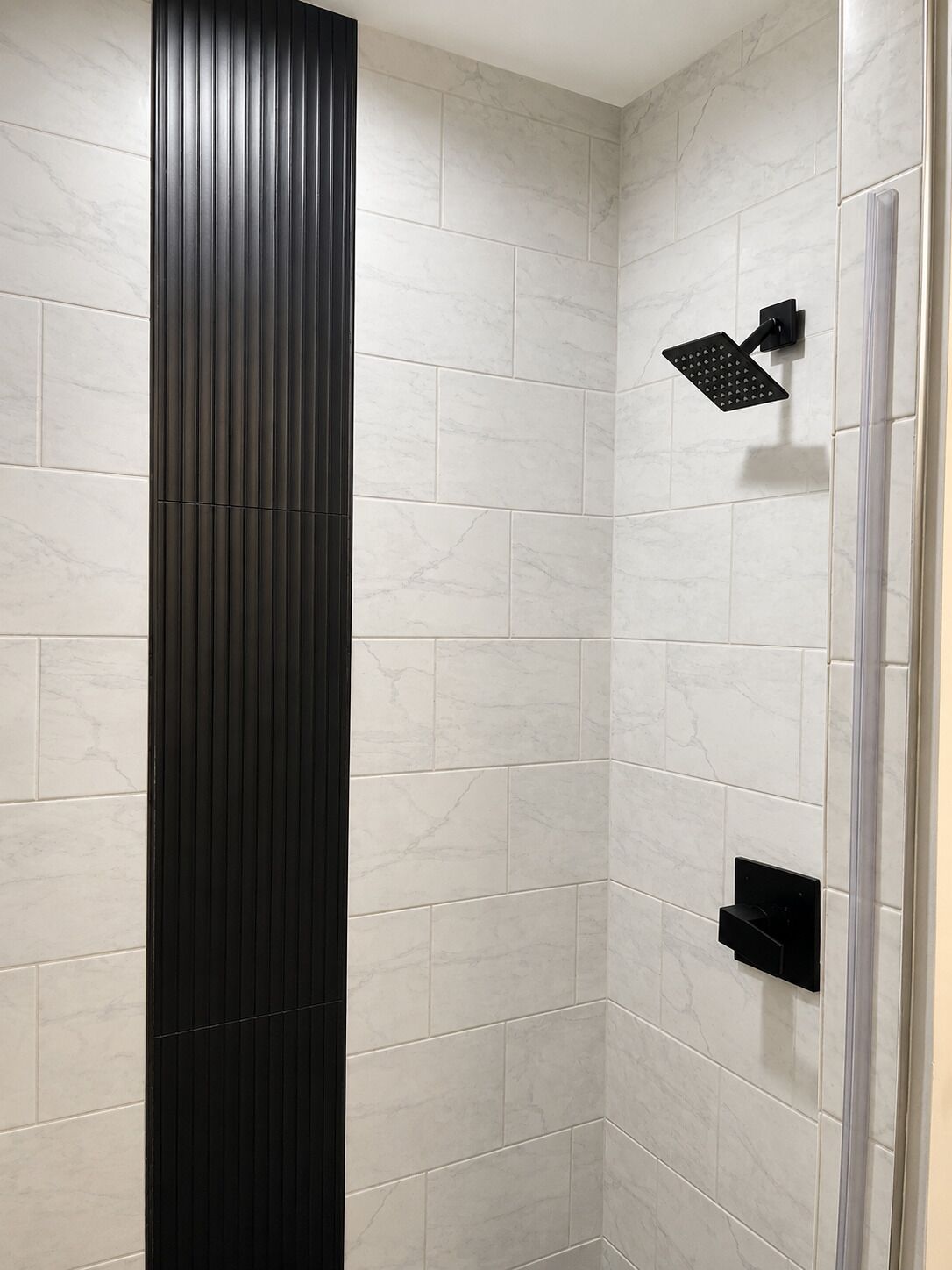 Una doccia moderna con pannello verticale nero, piastrelle in marmo bianco e soffione a mano.