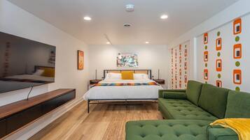 A modern bedroom with a bed, green sofa, and a TV on a wooden platform.