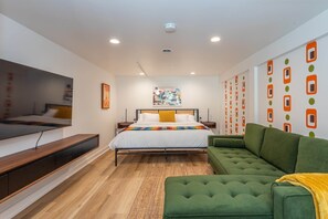 A modern bedroom with a bed, green sofa, and a TV on a wooden platform.