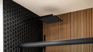 A modern bathroom with a black hexagonal tile wall, a wooden slatted wall, and a white sink.