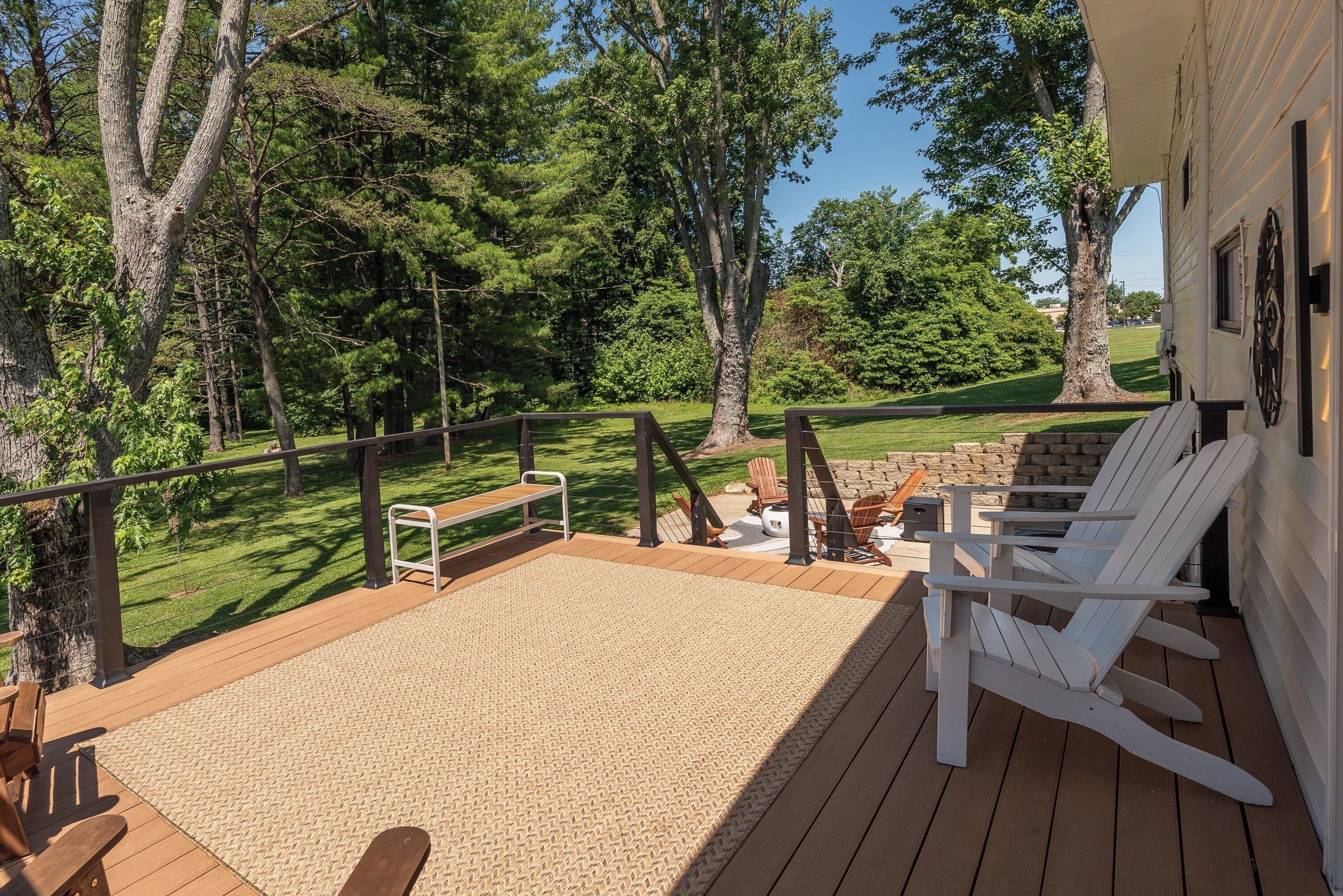 A deck with a wooden floor, white Adirondack chairs, a small table, and a bench.