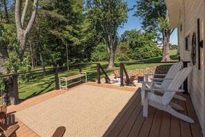 A deck with a wooden floor, white Adirondack chairs, a small table, and a bench.