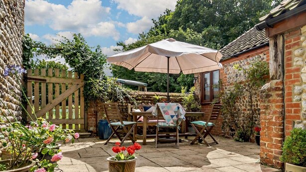 A patio with a table and chairs, a large umbrella, and potted plants. - 2 Bed in Thorpe Market (oc-kt107) (Thorpe Market)
