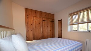 Ein Schlafzimmer mit Bett, Holzschrank und einem Fenster mit Jalousien.