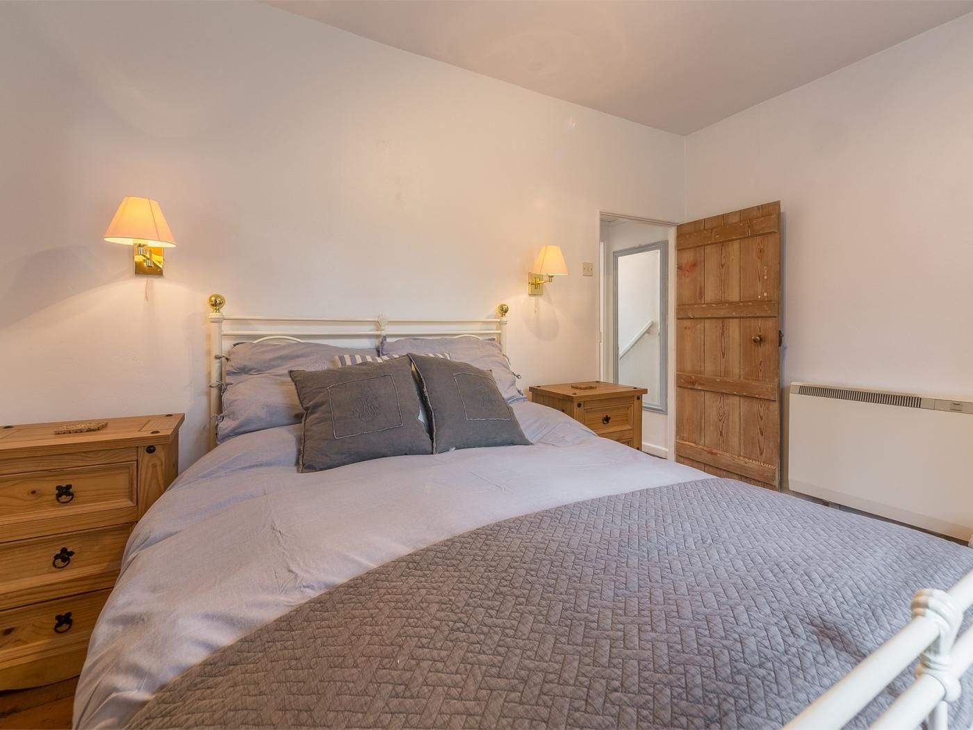 A bedroom with a bed, two bedside tables, a wooden wardrobe, and wall-mounted lamps.