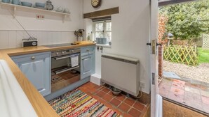 Een keuken met een houten aanrecht, blauwe kastjes, een fornuis en een raam met uitzicht op de tuin.
