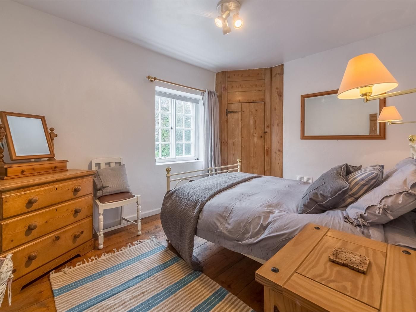 A bedroom with a bed, a dresser, a nightstand, a window, and a mirror.