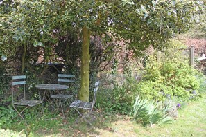 A garden with a metal table and chairs, surrounded by greenery and a tree. - 2 Bed in North Creake (oc-kt003) (North Creake)
