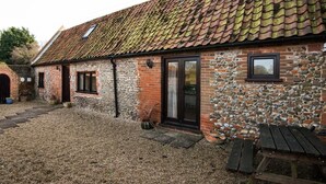 Un bâtiment rustique avec un toit en tuiles, des murs en pierre, une porte en bois et une petite fenêtre.