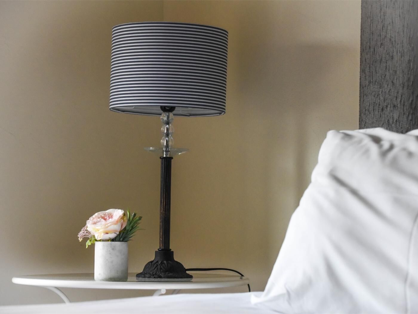 A lamp with a black base and a striped lampshade on a white table.