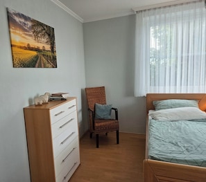 Ein Schlafzimmer mit einem Bett, einem Sessel, einer Kommode und einem Bild an der Wand.