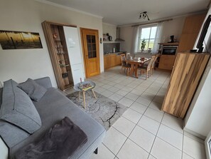 Ein Wohnzimmer mit grauem Sofa, einem kleinen runden Tisch und einer Küchenzeile mit Holdelementen und einem Esstisch.