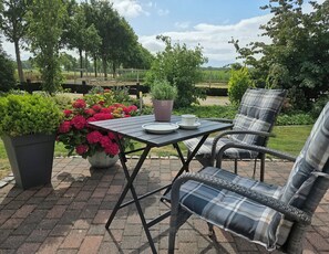 Eine Terrasse im Freien mit Tisch und zwei Stühlen, umgeben von Blumentöpfen und Blumen.