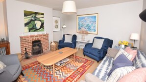 A living room with a fireplace, blue sofas, a wooden coffee table, and a colorful rug. - 3 Bed in Kettlestone (oc-kt037) (Little Snoring)