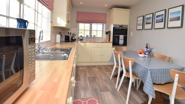 A kitchen with a wooden countertop, a sink, a stove, and a dining area with a table and chairs. - 3 Bed in Kettlestone (oc-kt037) (Little Snoring)