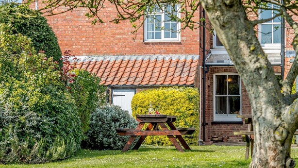 A brick building with a tiled roof, a wooden table, and a well-maintained garden. - 3 Bed in Thornham (oc-kt022) (Thornham)