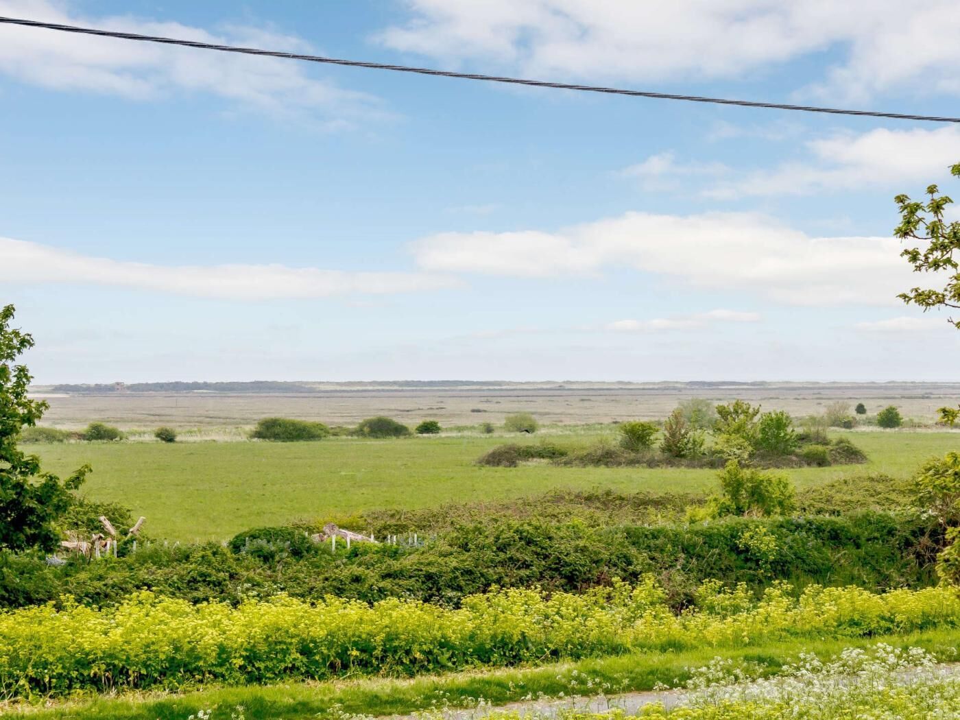 Et landligt landskab med åbne marker, spredte træer og en klar himmel.