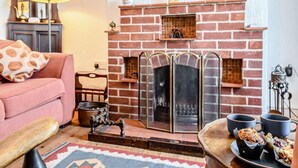 A cozy living room with a brick fireplace, a pink sofa, a wooden bench, and a tray with pastries. - 3 Bed in Thornham (oc-kt022) (Thornham)