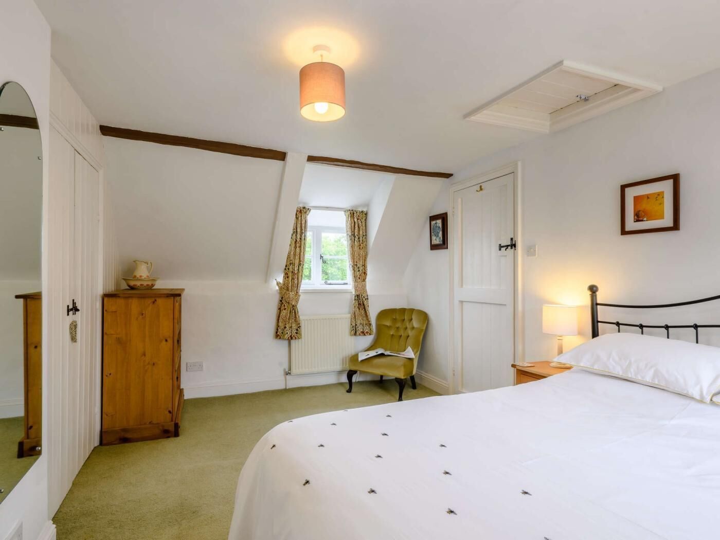 Ein Schlafzimmer mit einem Bett, einem Sessel, einer Holzkabine, einem Fenster mit Vorhängen und einer Deckenleuchte.