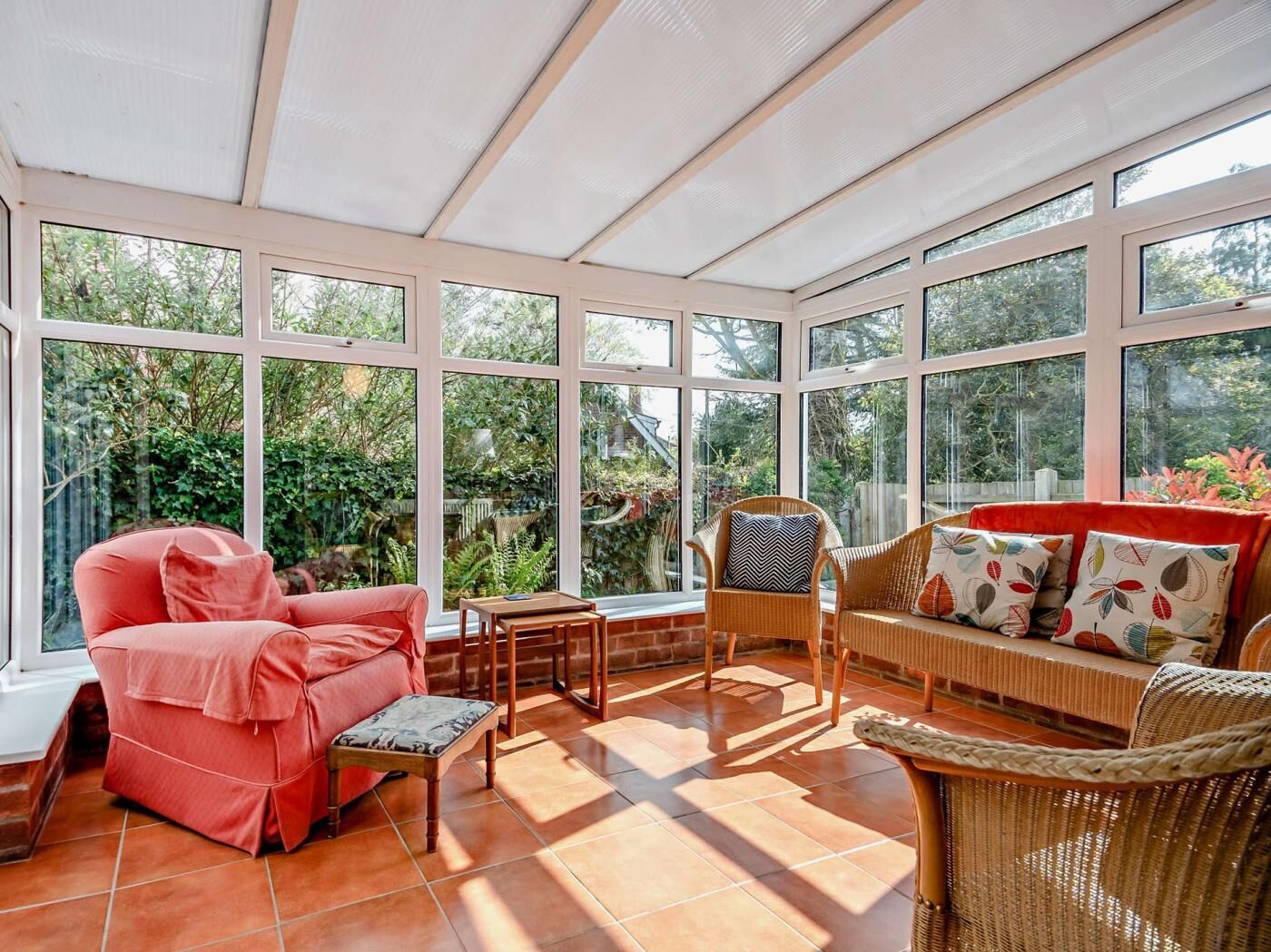 A conservatory with large windows, a red sofa, wicker chairs, and a small table.