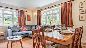 Ein Essbereich mit einem Holztisch, gedeckt für vier Personen, einem blauen Sofa mit gemusterten Kissen und großen, mit Vorhängen versehenen Fenstern.
