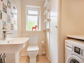 Een badkamer met toilet, wastafel, raam en wasmachine.