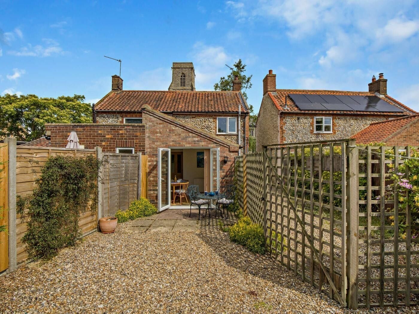 A residential property with a gravel driveway, a wooden fence, and a patio area with outdoor furniture.