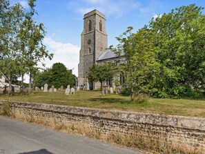 A church with a tall tower, a cemetery with headstones, and a stone wall. - 2 Bed in Trunch (oc-kt035) (Trunch)