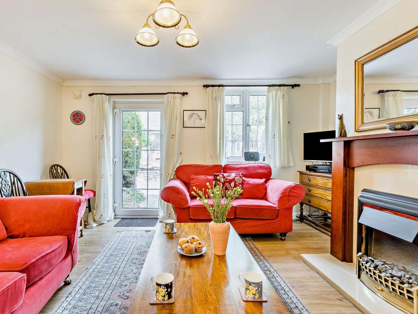A living room with a red sofa, a wooden coffee table with a vase and muffins, a fireplace, and a television.