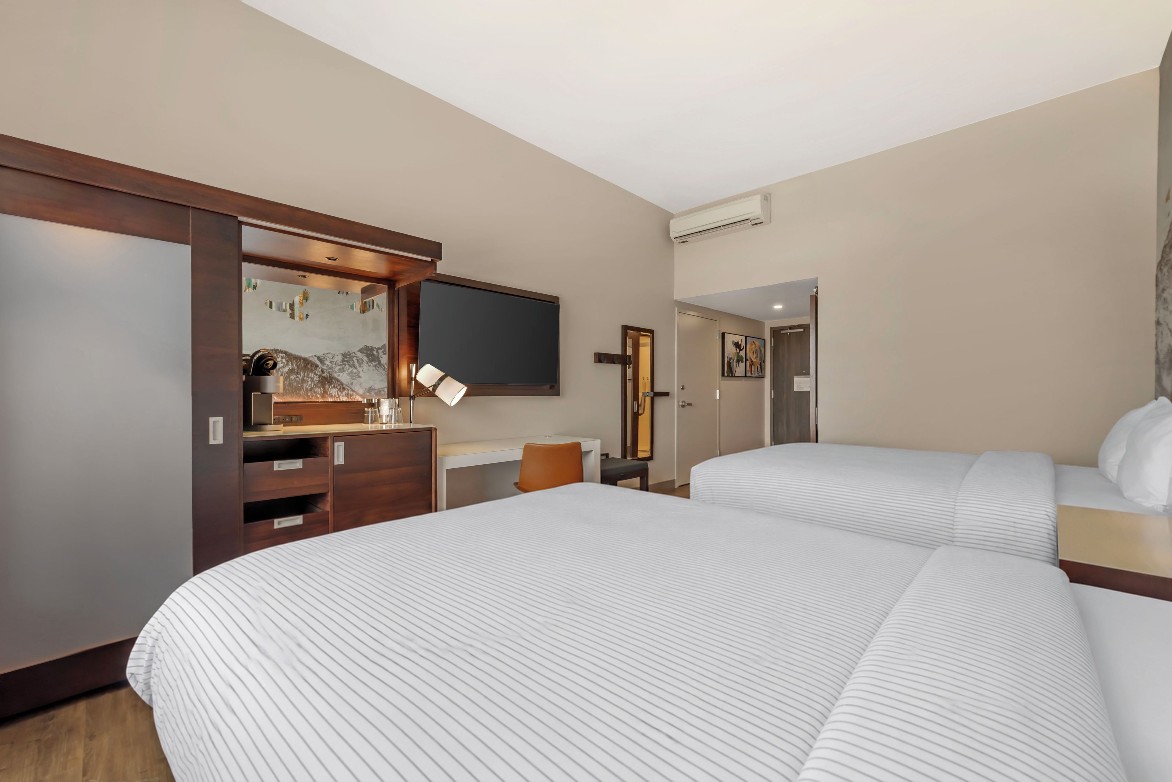 Une chambre d’hôtel avec deux lits, un bureau, une chaise, une télévision et une armoire.