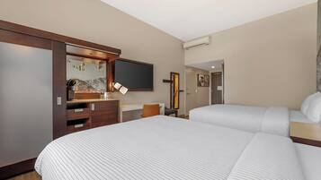 Une chambre d’hôtel avec deux lits, un bureau, une chaise, une télévision et une armoire.