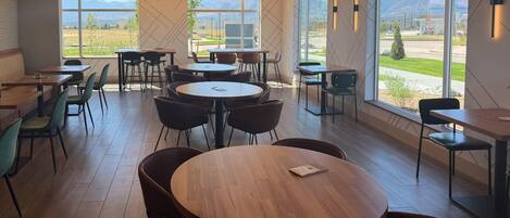 A modern cafe interior with round tables, chairs, and large windows offering a view of the outdoors.