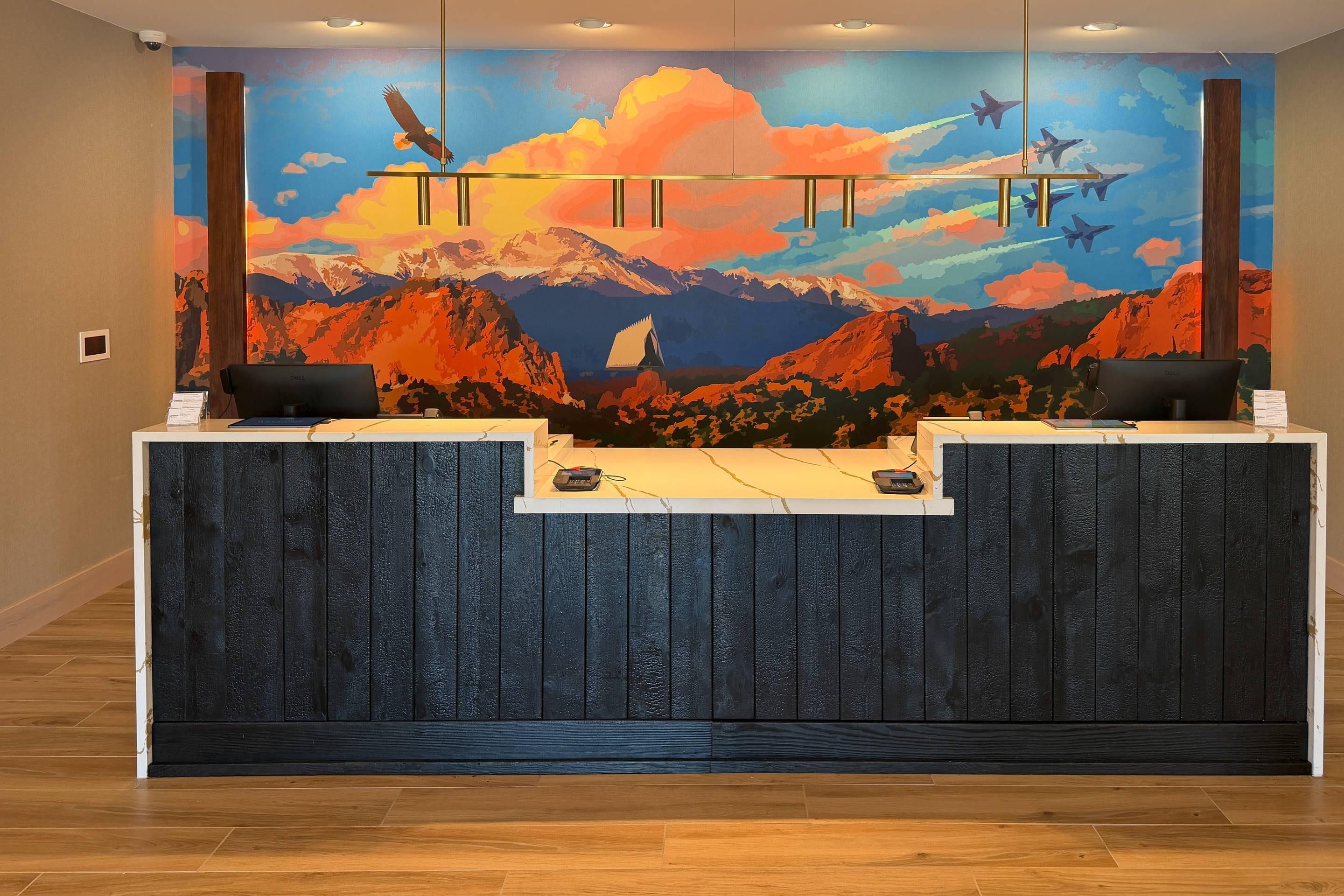 Un mostrador de recepción con un mural de montañas y aviones, dos sillas negras y suelo de madera.