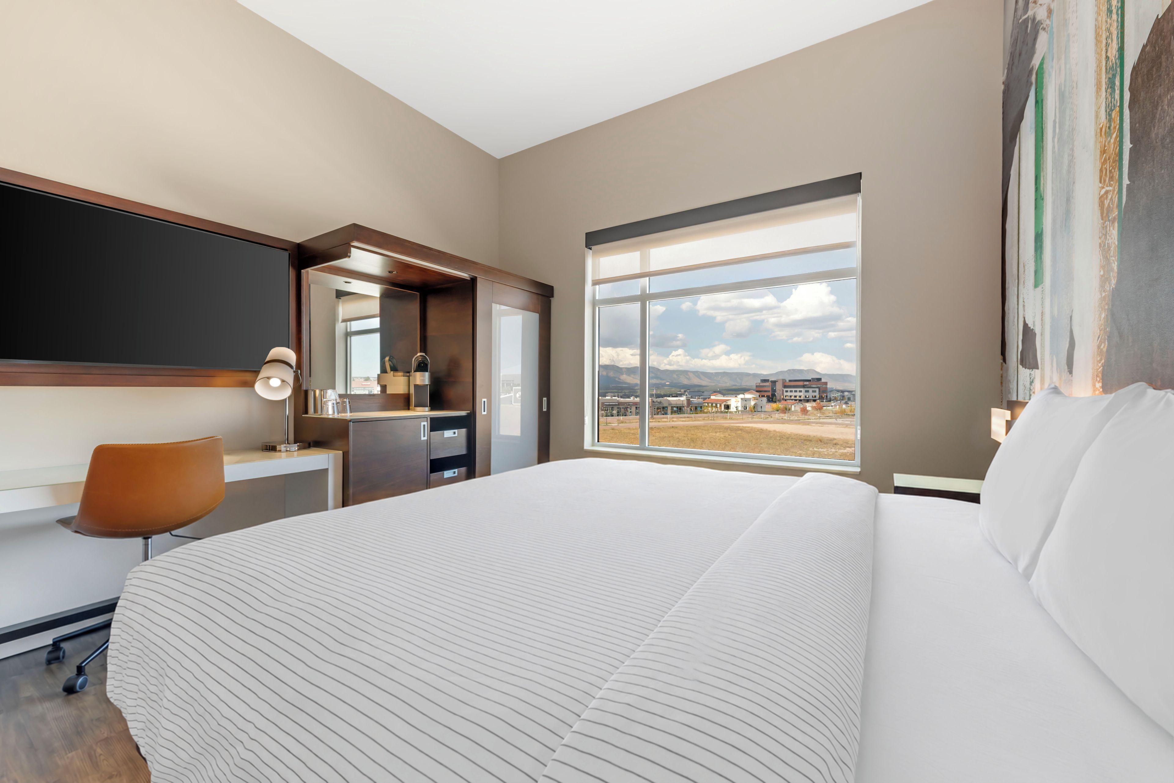 Ein modernes Hotelzimmer mit einem großen Bett, einem Schreibtisch, einem Stuhl und einem Fenster mit Blick auf die Stadt.
