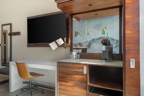 Una habitación de hotel con un escritorio de madera, una silla, un televisor de pantalla plana, una cafetera y un detalle decorativo en la pared.