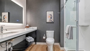 Un baño moderno con un lavamanos blanco, un inodoro, una ducha y dos cuadros en la pared.