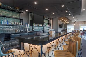 A bar area with a long counter, multiple shelves of bottles, and bar stools. - Cambria Hotel Colorado Springs - Air Force Academy (Colorado Springs)
