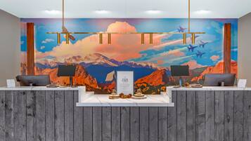 A reception desk with two computer monitors, a wooden reception desk, and a mural of mountains and airplanes.