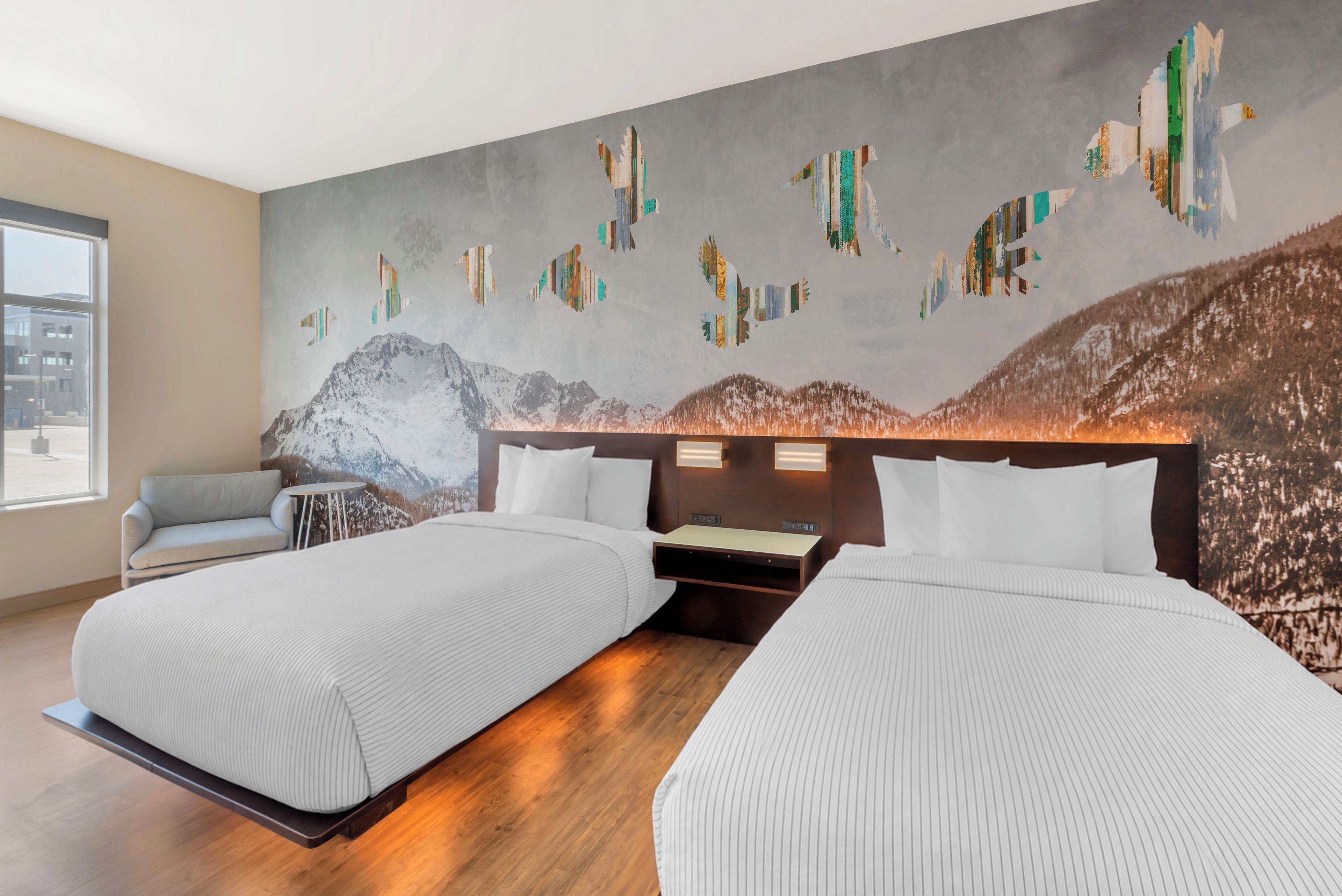 Une chambre d’hôtel avec deux lits, un canapé, une petite table et une fresque murale.