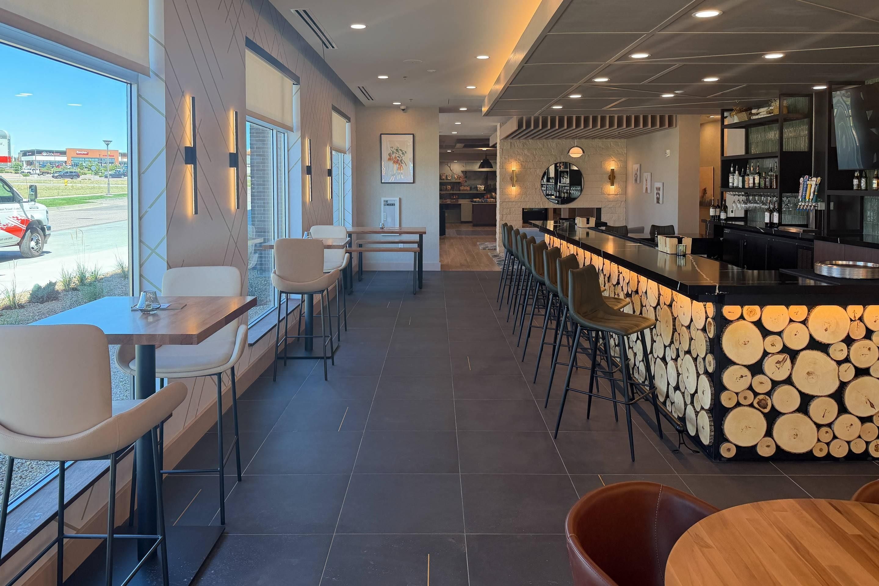 Un espace bar moderne, doté d’un comptoir, de sièges et offrant une vue sur l’extérieur.