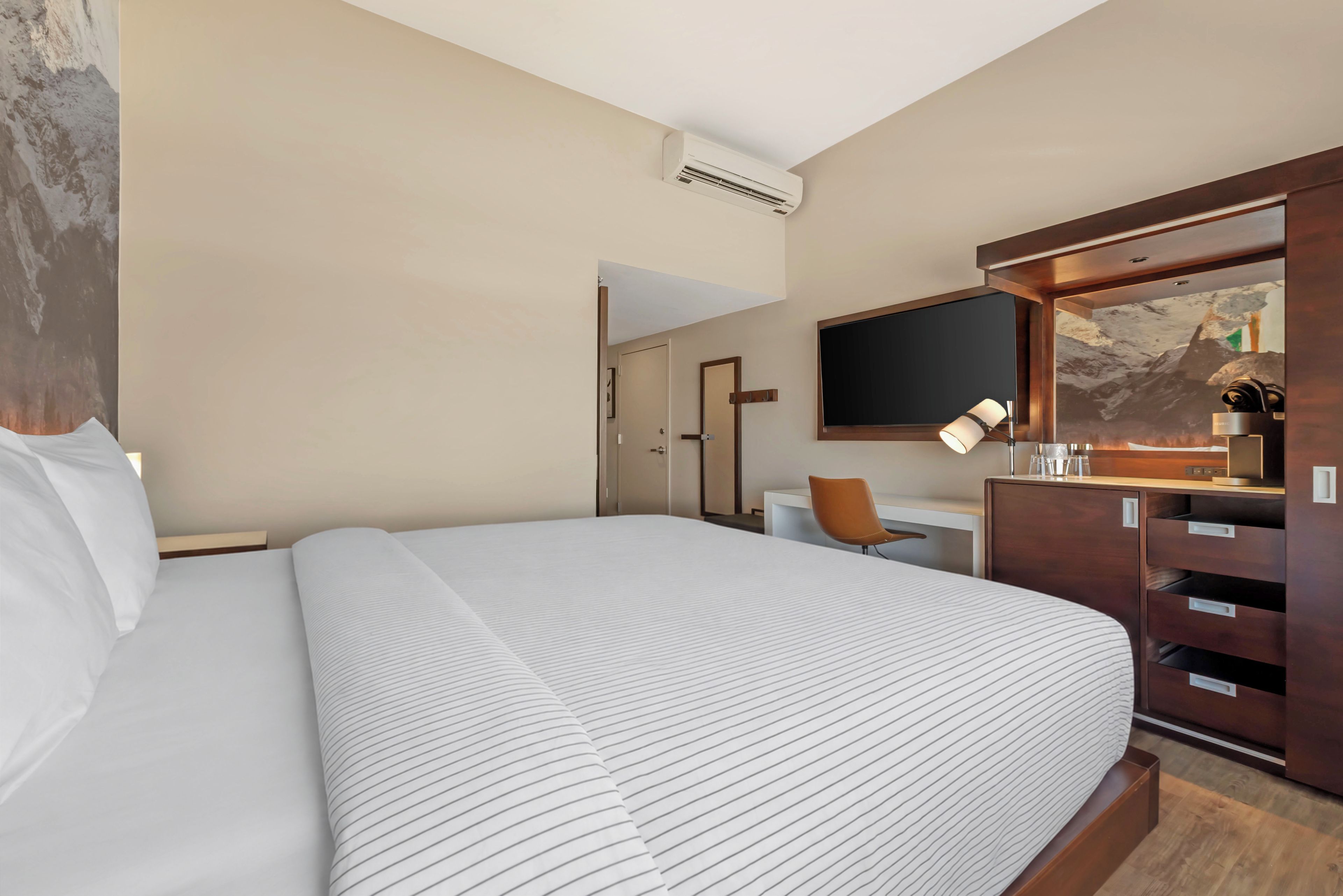 Habitación de hotel con una cama grande, un escritorio con silla, televisión y armario.