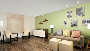 A modern living room with a sofa, armchairs, ottomans, a coffee table, and a side table with a lamp. - Woodspring Suites (Glendale)