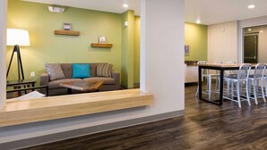 A modern living area with a sofa, coffee table, and a dining table with chairs. - Woodspring Suites (Glendale)