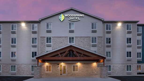 A multi-story hotel with a stone facade, a prominent entrance with a wooden canopy, and a sign reading 'WOODSPRING SUITES'. - Woodspring Suites (Glendale)