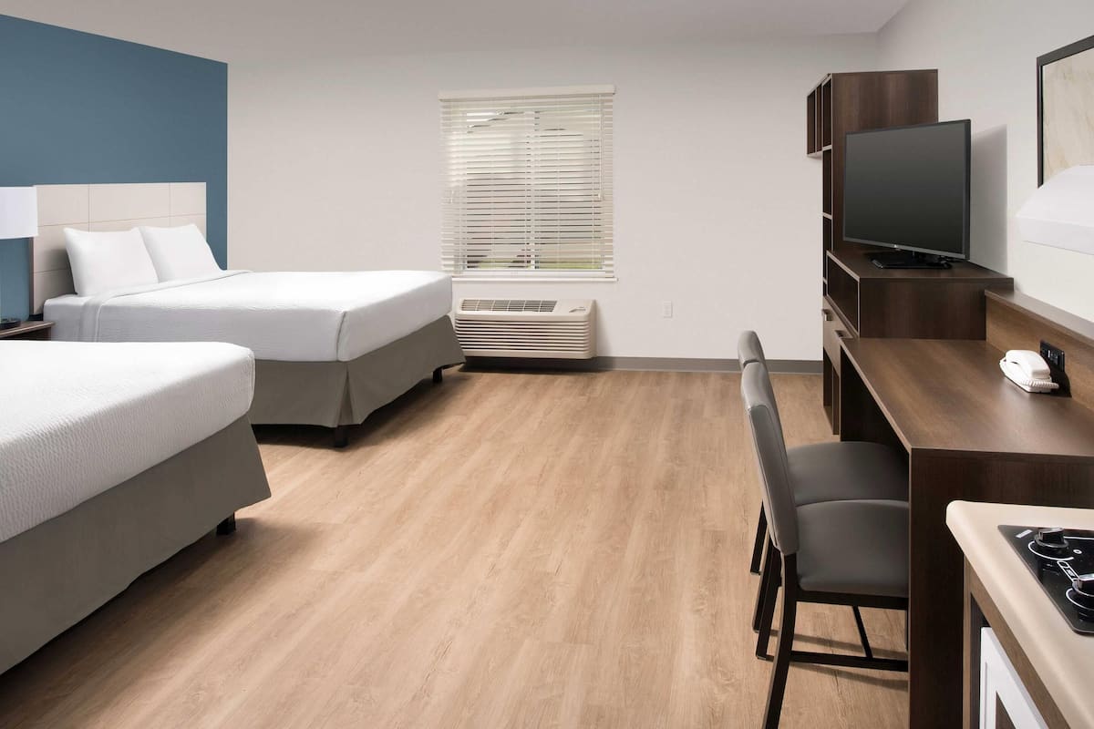 Habitación de hotel con dos camas, un escritorio con silla, televisión y ventana con persianas.