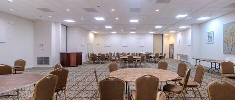 A conference room with multiple tables and chairs, carpeted floor, and ceiling lights.