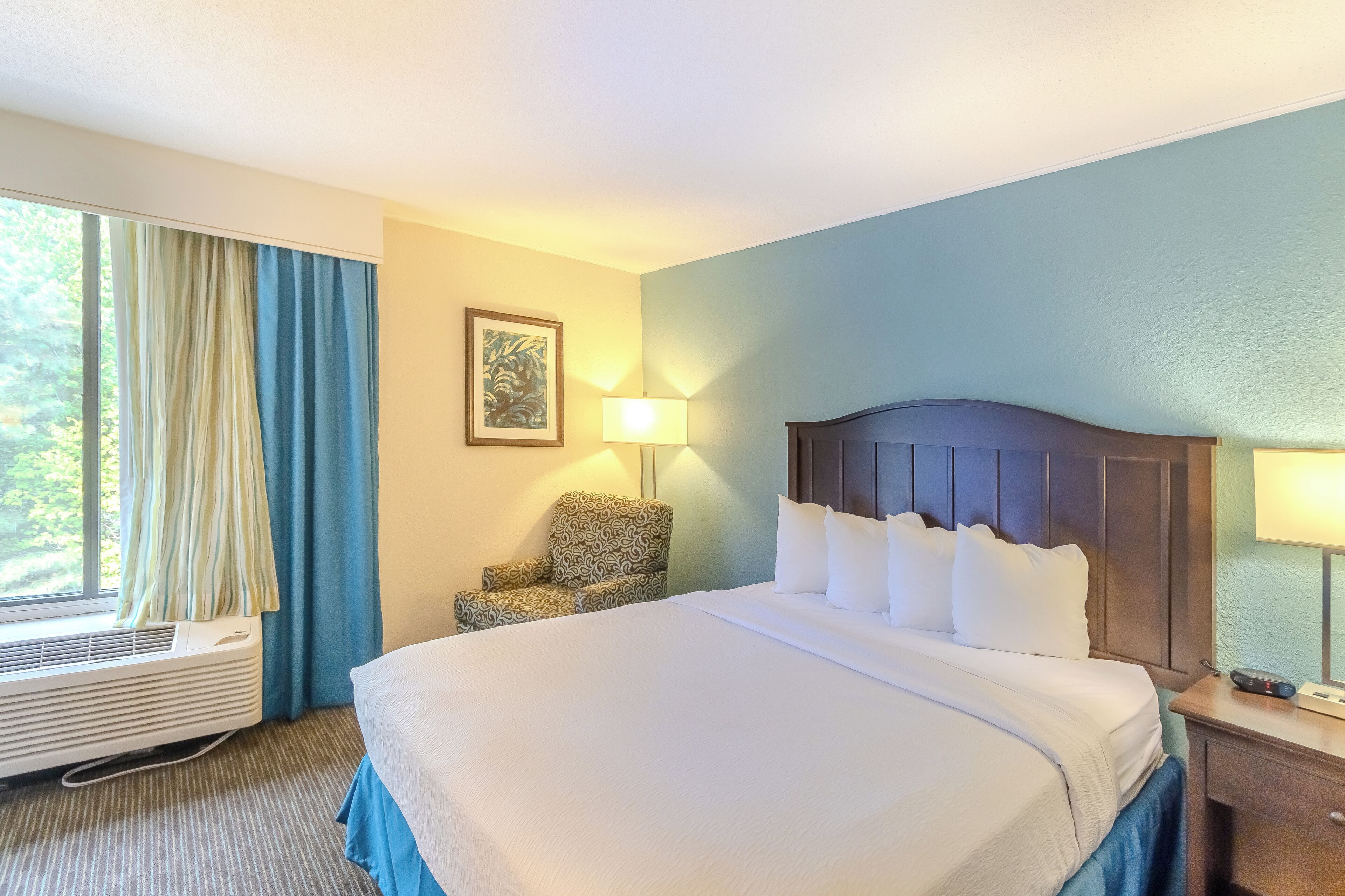Habitación de hotel con cama, una silla, una lámpara y una ventana con cortinas.